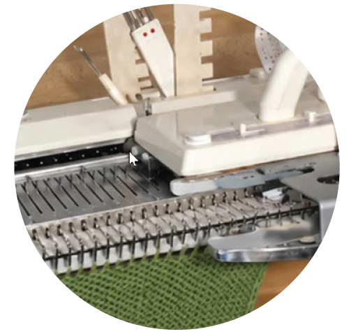A knitting machine in progress with green fabric on the needles